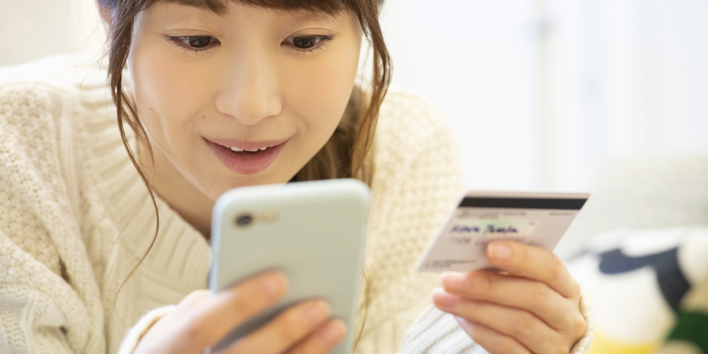 スマホの画面とクレカを見る女性