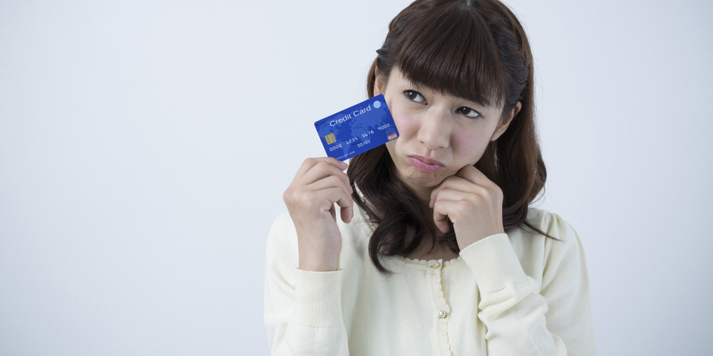クレカを手に持って何かに悩む女性