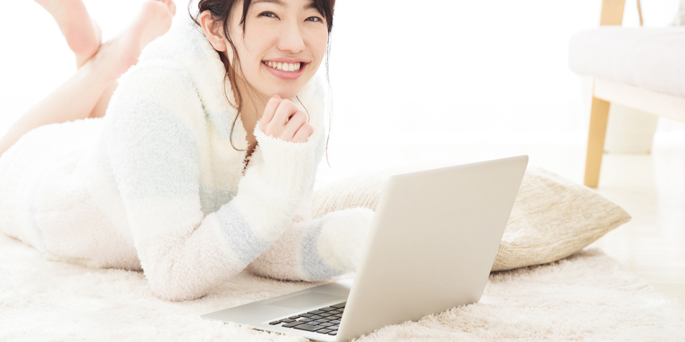 寝転んでノートPCをいじる女性