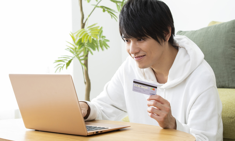 ノートパソコンを見ながらクレカを持つ男性