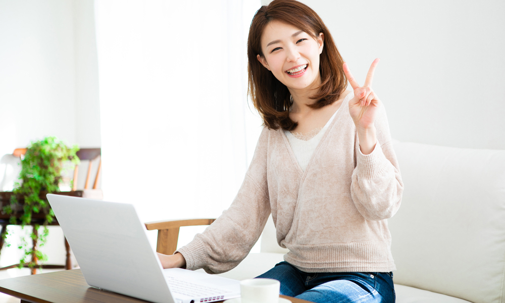 ノートパソコンの前でピースする女性