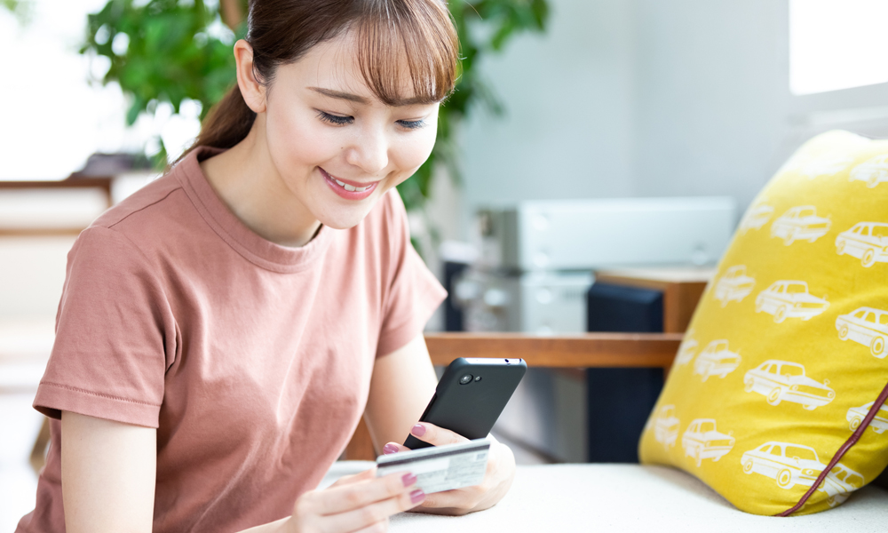 スマホを操作しながらクレカを見る女性