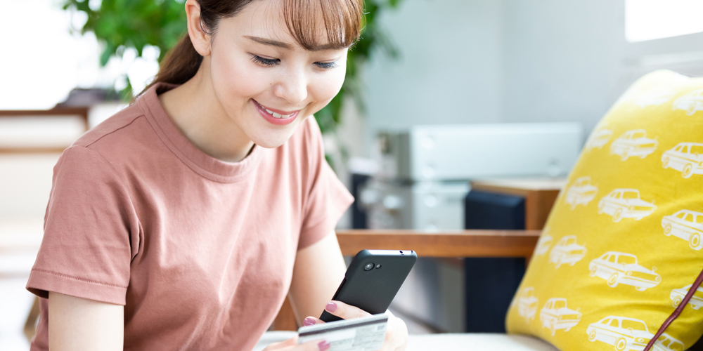 クレジットカード片手にスマホを操作する女性
