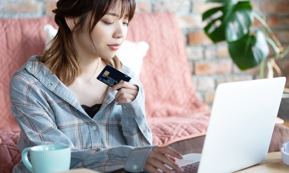 クレカを持ちながらノートPCを見つめる女性