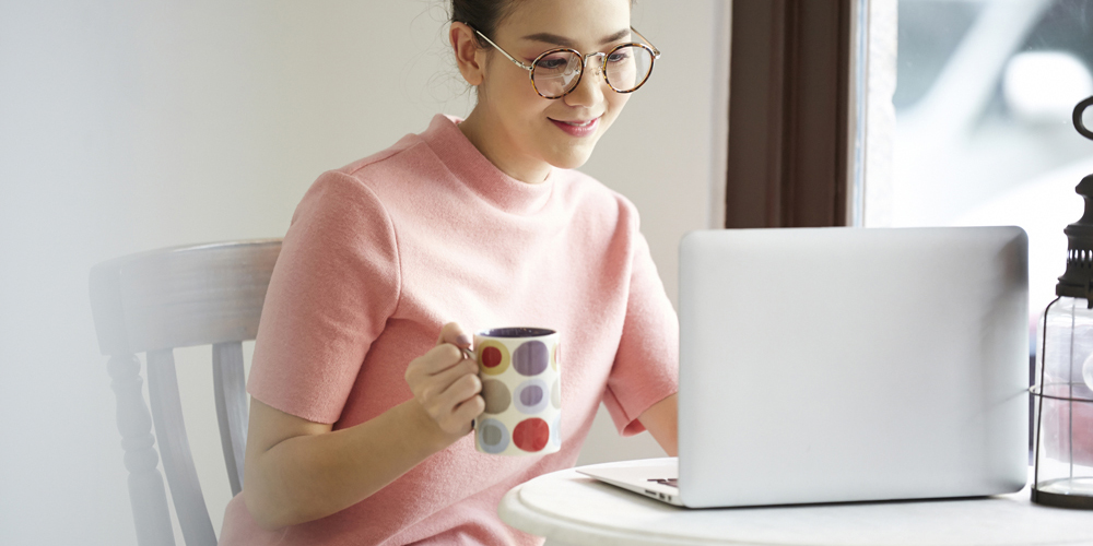 マグカップ片手にノートPCをいじる女性