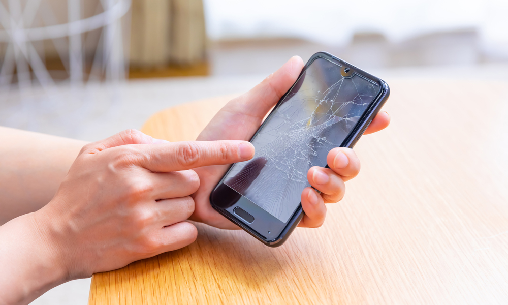 画面が割れたスマホを指差す人
