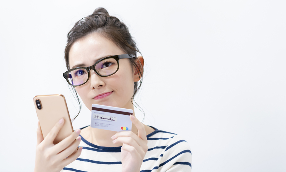 スマホとクレカを持って悩む眼鏡の女性