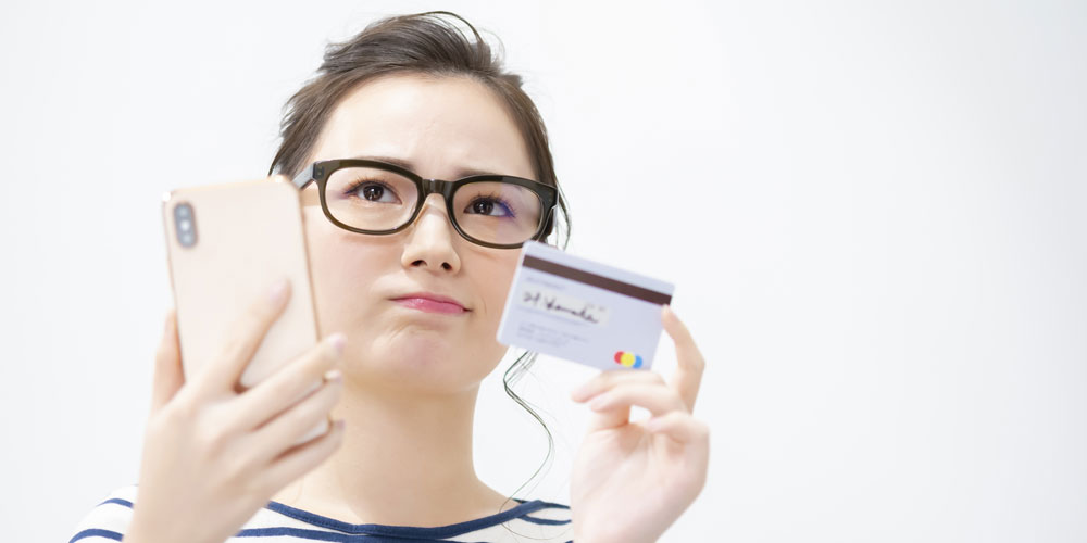 スマホとクレカを持って悩む眼鏡の女性
